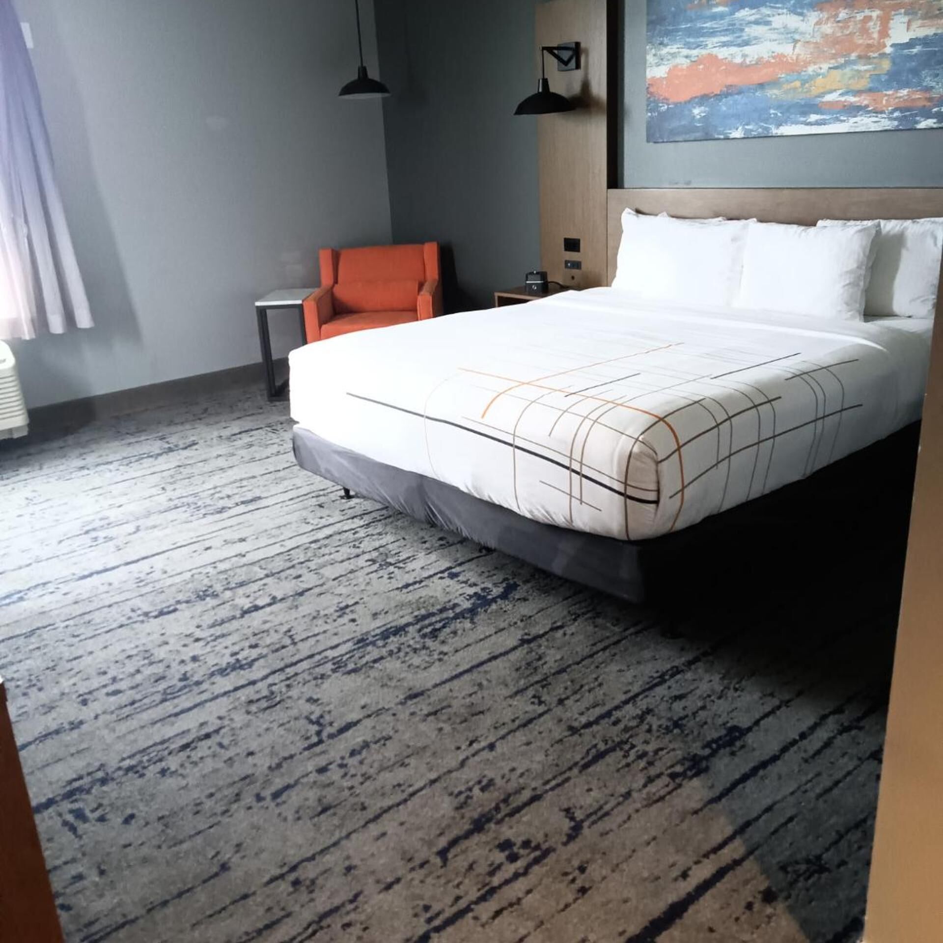 A hotel room with a large bed, a chair, a desk, and a painting on the wall.