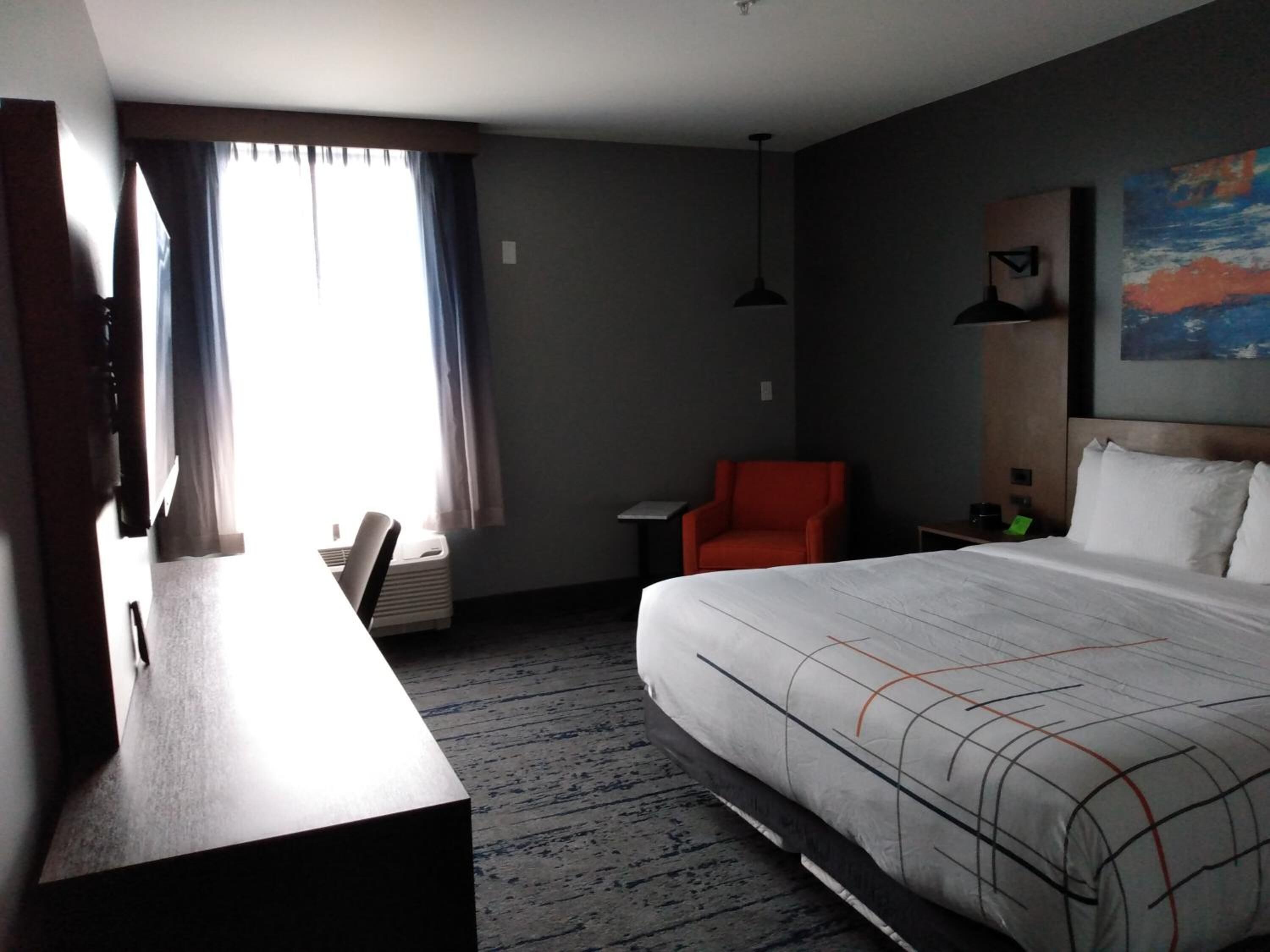 Una habitación de hotel con una cama, un escritorio, una silla, una mesita y un cuadro en la pared.
