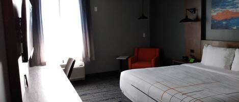 Una habitación de hotel con una cama, un escritorio, una silla, una mesita y un cuadro en la pared.