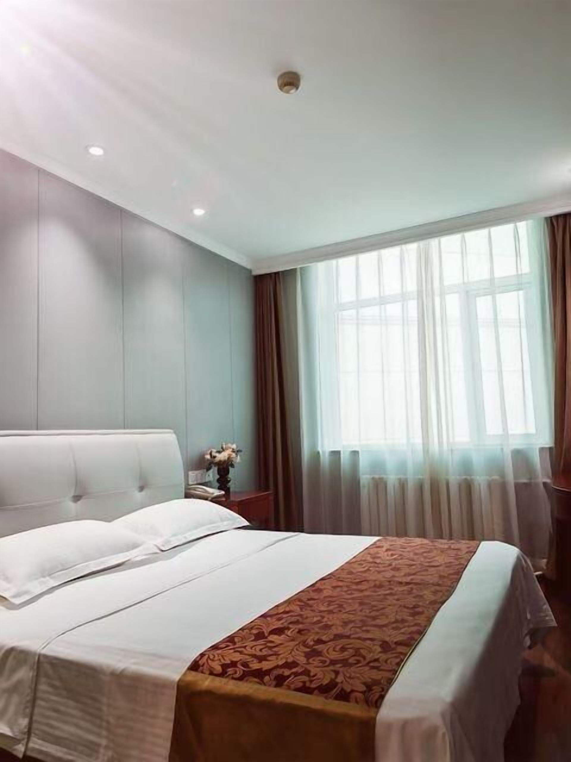 Habitación de hotel con una cama grande, una mesita de noche, una lámpara, una ventana con cortinas y una luz en el techo.
