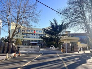 Un cancello chiuso con un edificio sullo sfondo, cielo sereno e alberi.