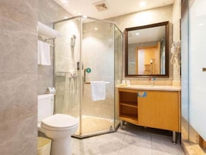 Un baño con ducha de vidrio, inodoro, lavamanos con espejo y una toalla colgada en la pared.