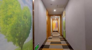 A hallway with a checkered floor, a wall mural of a tree, and a door at the end. - Shell Hotel (Wuxi)