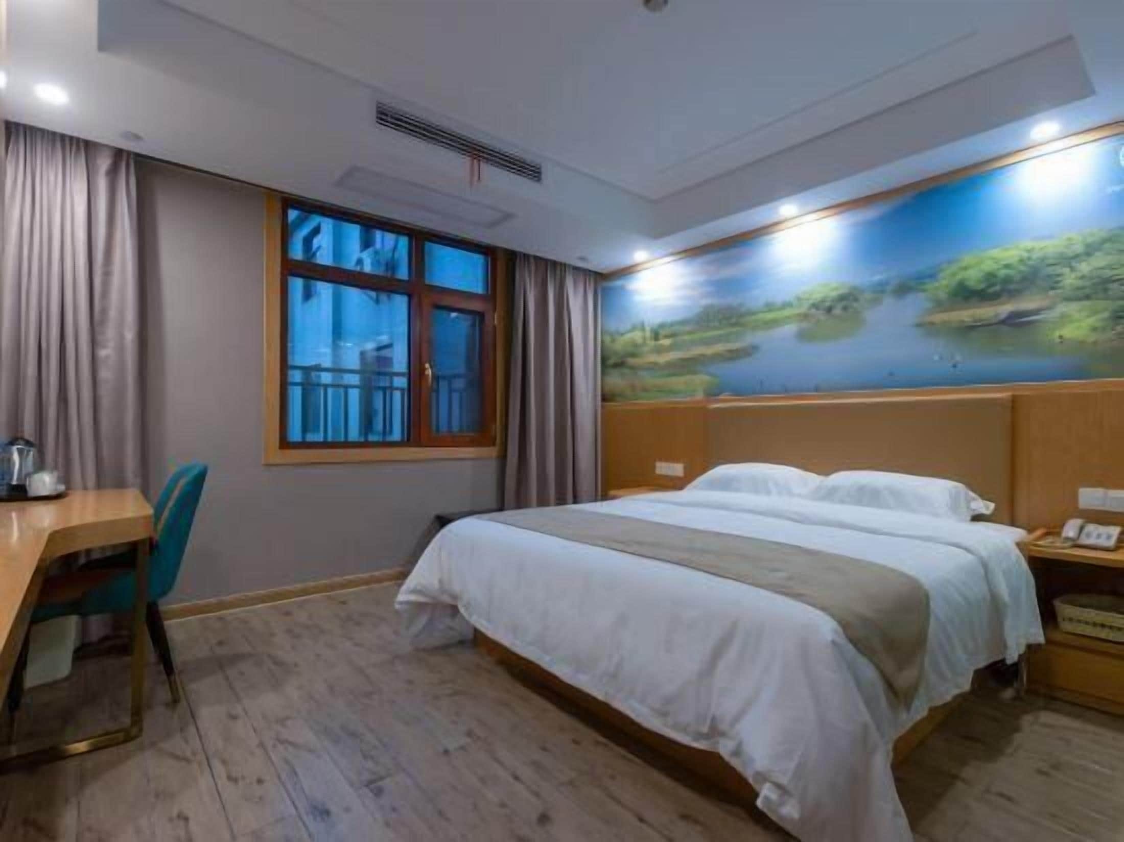Habitación de hotel con cama, un escritorio con silla, una ventana con cortinas y un cuadro de un paisaje en la pared.