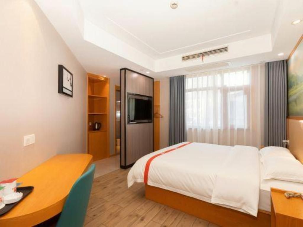 A hotel room with a bed, a desk, a television, and a window with curtains.