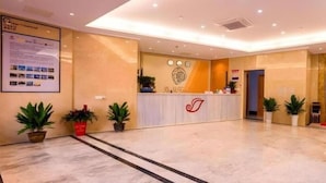 A hotel reception area with a reception desk, potted plants, and a wall-mounted sign. - Shell Hotel (Wuxi)
