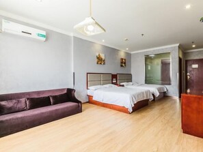 A hotel room with a wooden floor, a bed with white bedding, a purple sofa, and a ceiling light fixture.