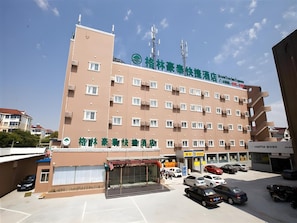 A multi-story hotel with a flat facade, multiple windows, and a parking area with several cars. - Greentree Inn Shanghai Huinan Jinghai Road Express Hotel (Shanghai)