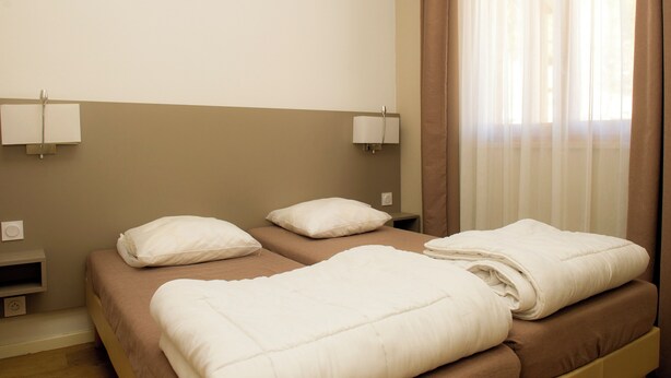 Ein Hotelzimmer mit zwei Betten, jeweils mit weißer Bettwäsche und Kissen, einem Nachttisch und einer Wandlampe.