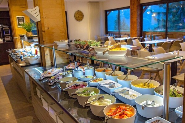 Ein reichhaltiges Buffet mit verschiedenen Speisen und Besteck, in einem Raum mit Holzwänden und großen Fenstern.