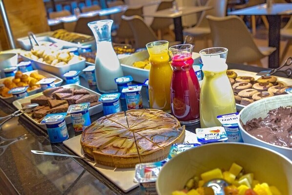 Een buffet met diverse etenswaren, waaronder een groot stuk taart, vruchtensappen en yoghurt parfait.