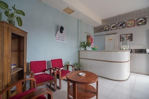 Un área de recepción con mostrador, sillas rojas, un mueble de madera y un calendario en la pared.