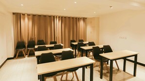 Una sala conferenze con diversi tavoli e sedie, pareti color beige e uno sfondo con tenda.