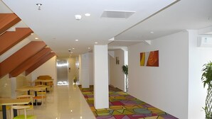 A modern interior with a colorful geometric floor design, wooden tables and chairs, and a staircase with a sloped ceiling. - Shell Shanghai Baoshan District Tieli Road Subway Station Tiefeng Road Hotel (Shanghai)
