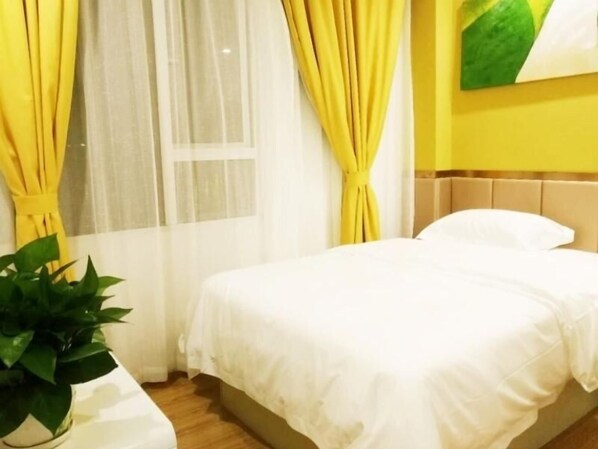 Une chambre d’hôtel avec un lit, des rideaux, une plante en pot et un mur orné d’un tableau représentant des feuilles.