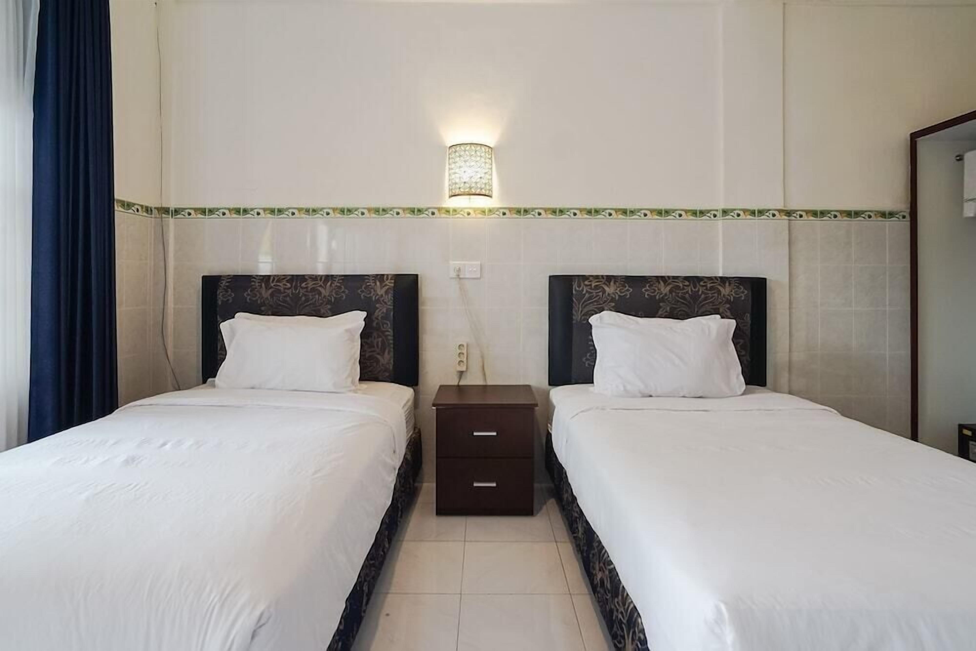 A hotel room with two beds, a nightstand between them, and a wall-mounted light fixture.