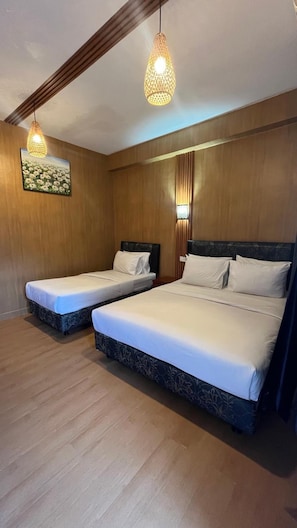 A hotel room with two beds, wooden paneling, and a painting on the wall. - City Garden Bali Dwipa Hotel (Kuta)