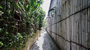 A narrow alley with a bamboo fence on one side and a brick pathway. - City Garden Bali Dwipa Hotel (Kuta)