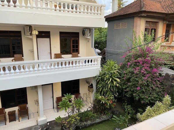 Ein zweistöckiges Gebäude mit Balkon, Außenbestuhlung und einem Garten mit verschiedenen Pflanzen und Blumen.