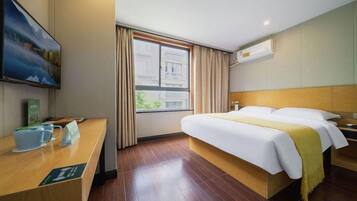 A hotel room with a wooden bed, a desk with a coffee cup, a window with curtains, and a painting on the wall.