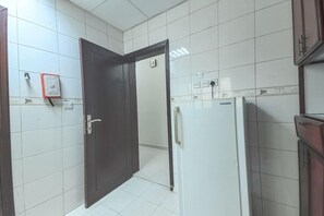 Une cuisine avec des murs recouverts de carreaux blancs, un réfrigérateur blanc et une porte en bois.