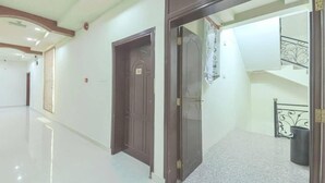 A hallway with two doors, a staircase, and a trash bin. - OYO 111 Al Thabit Hotel (Sur)
