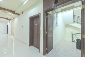 A hallway with two doors, a staircase, and a trash bin.