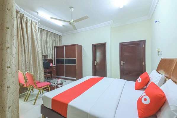 Une chambre d’hôtel équipée d’un lit, d’un bureau, d’une chaise, d’une armoire et d’un ventilateur de plafond.