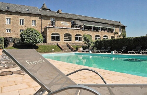 A pool area with lounge chairs and a building with arched windows and a balcony. - Le Chateau de Fontanges (Onet-le-Chateau)