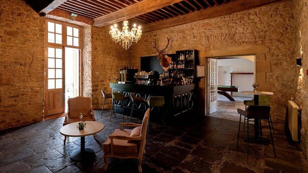A rustic interior with stone walls, a wooden ceiling, a chandelier, a bar area, and seating.