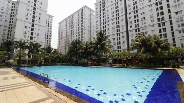 A swimming pool with a blue tiled edge, surrounded by palm trees and tall residential buildings. - Sewaunitkalcit (Jakarta)