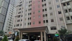 A multi-story building with a central entrance and several parked cars in front. - Sewaunitkalcit (Jakarta)