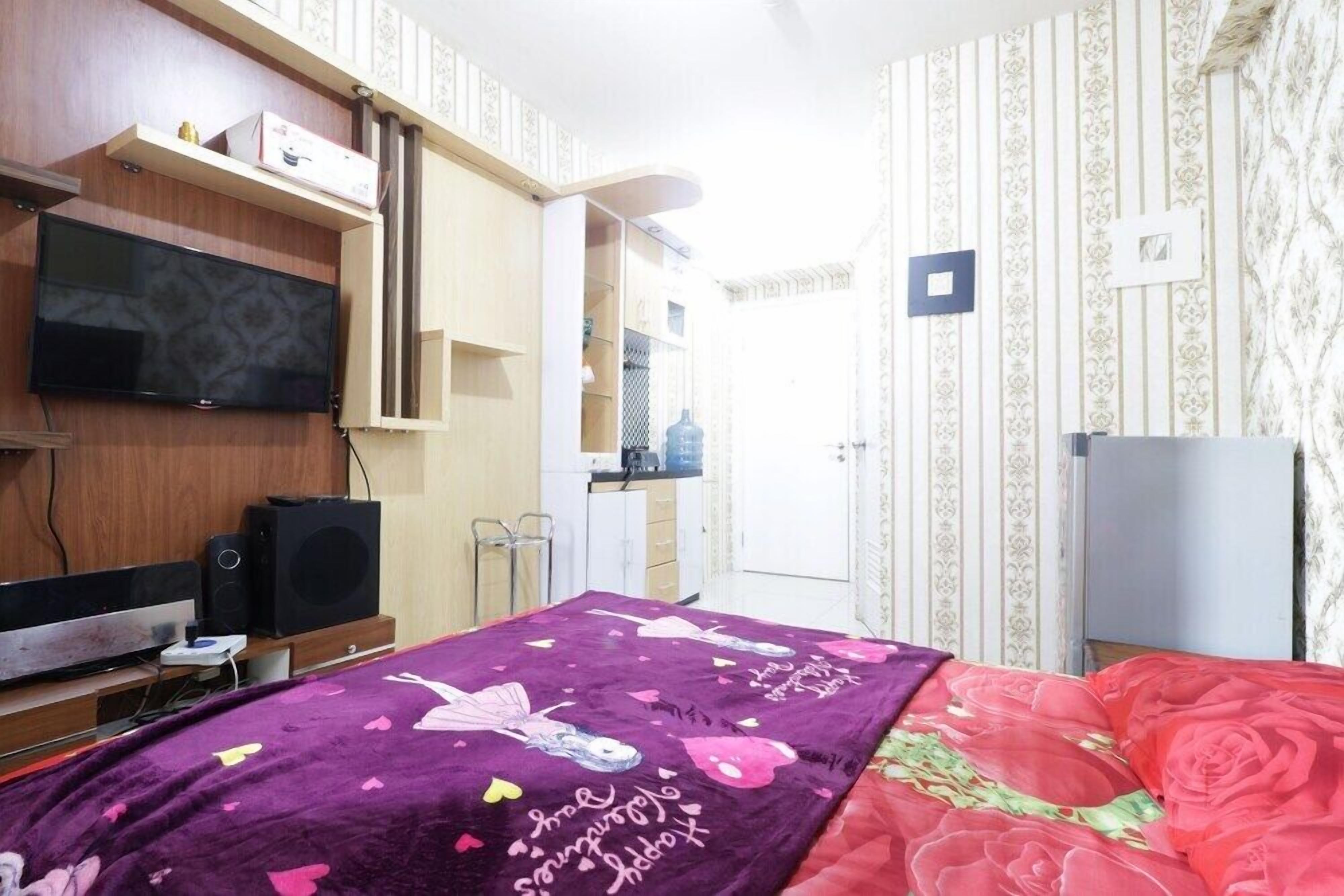 A bedroom with a bed, a TV, a wardrobe, and a small kitchenette.