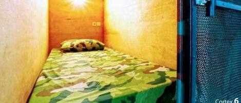 A small, enclosed room with a single bed, a door with a metal latch, and a wooden ceiling.