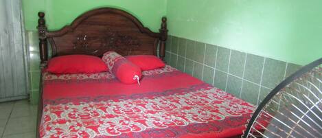 A bed with a red and white patterned bedspread, wooden headboard, and two red pillows.