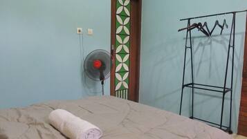 A room with a bed, a wall-mounted fan, a door with a geometric pattern, and a metal rack with clothes.