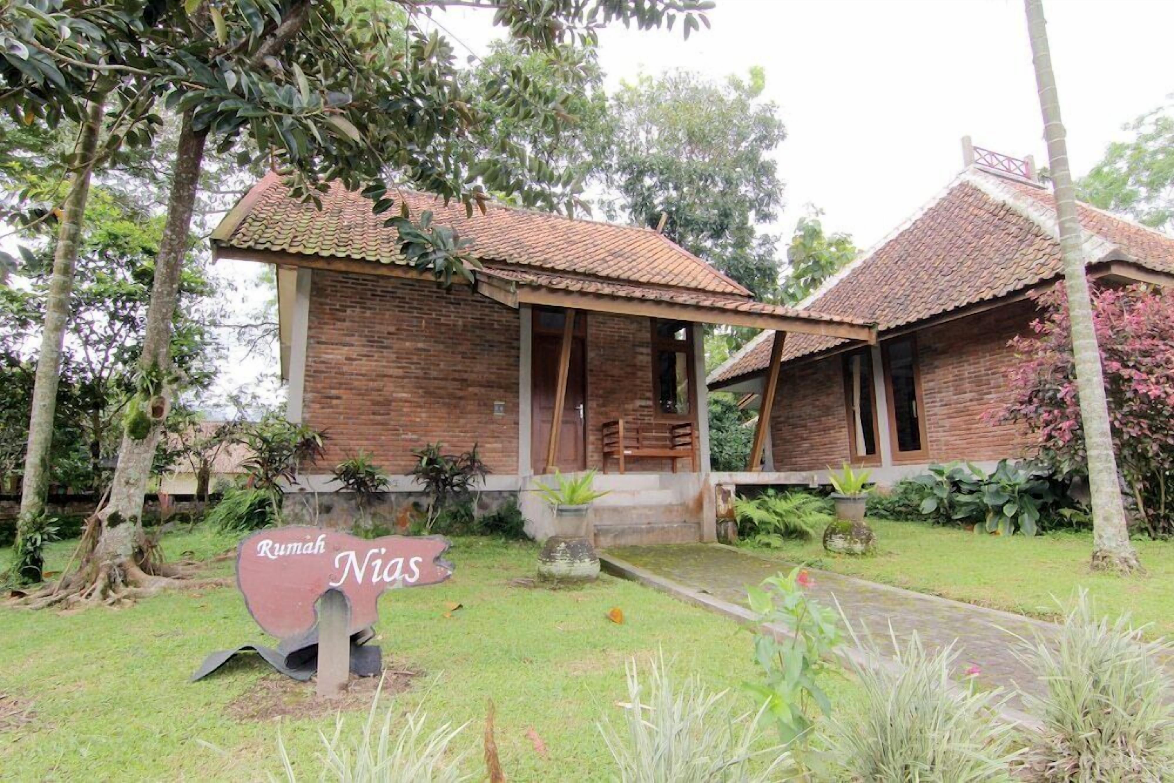 A traditional brick house with a tiled roof, surrounded by lush greenery and a sign reading "Rumah Nias".
