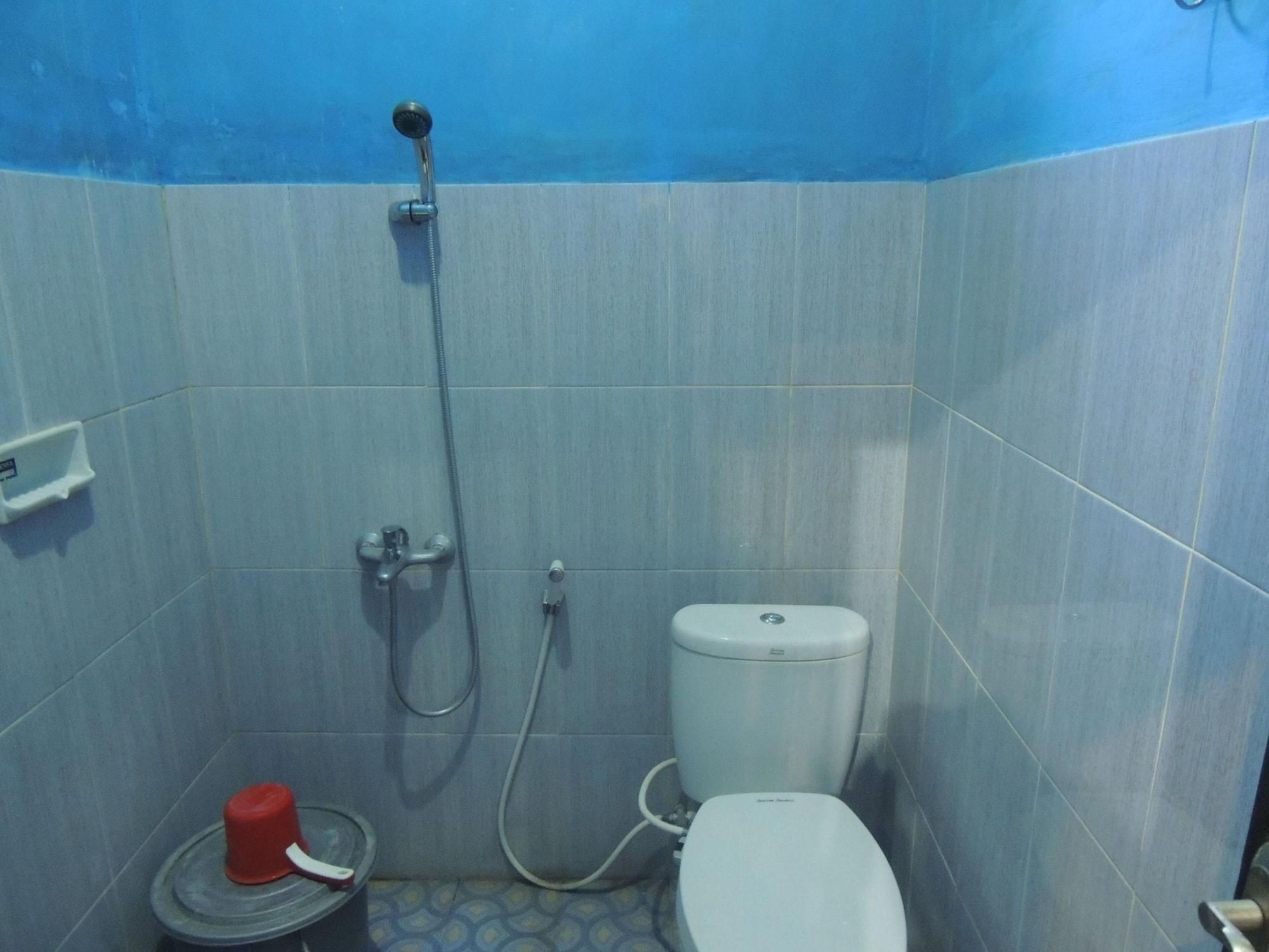 A small bathroom with a toilet, a shower, and a red bucket.