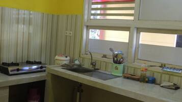 A kitchen with a gas stove, sink, window, and a gas cylinder.