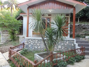 A house with a stone facade, wooden porch, and a small garden with a palm tree. - Homestay Alam Baru by Zuzu (Wonosari)
