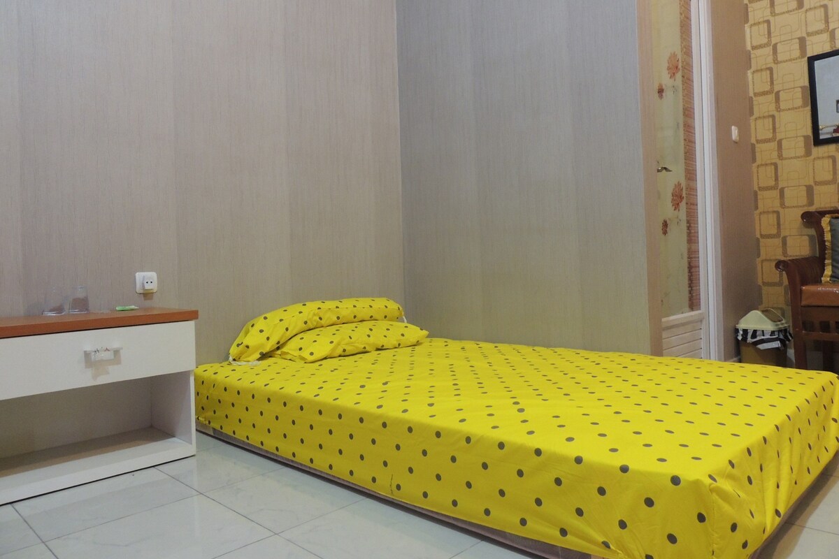 A small bedroom with a bed, a nightstand, a dresser, and a door.