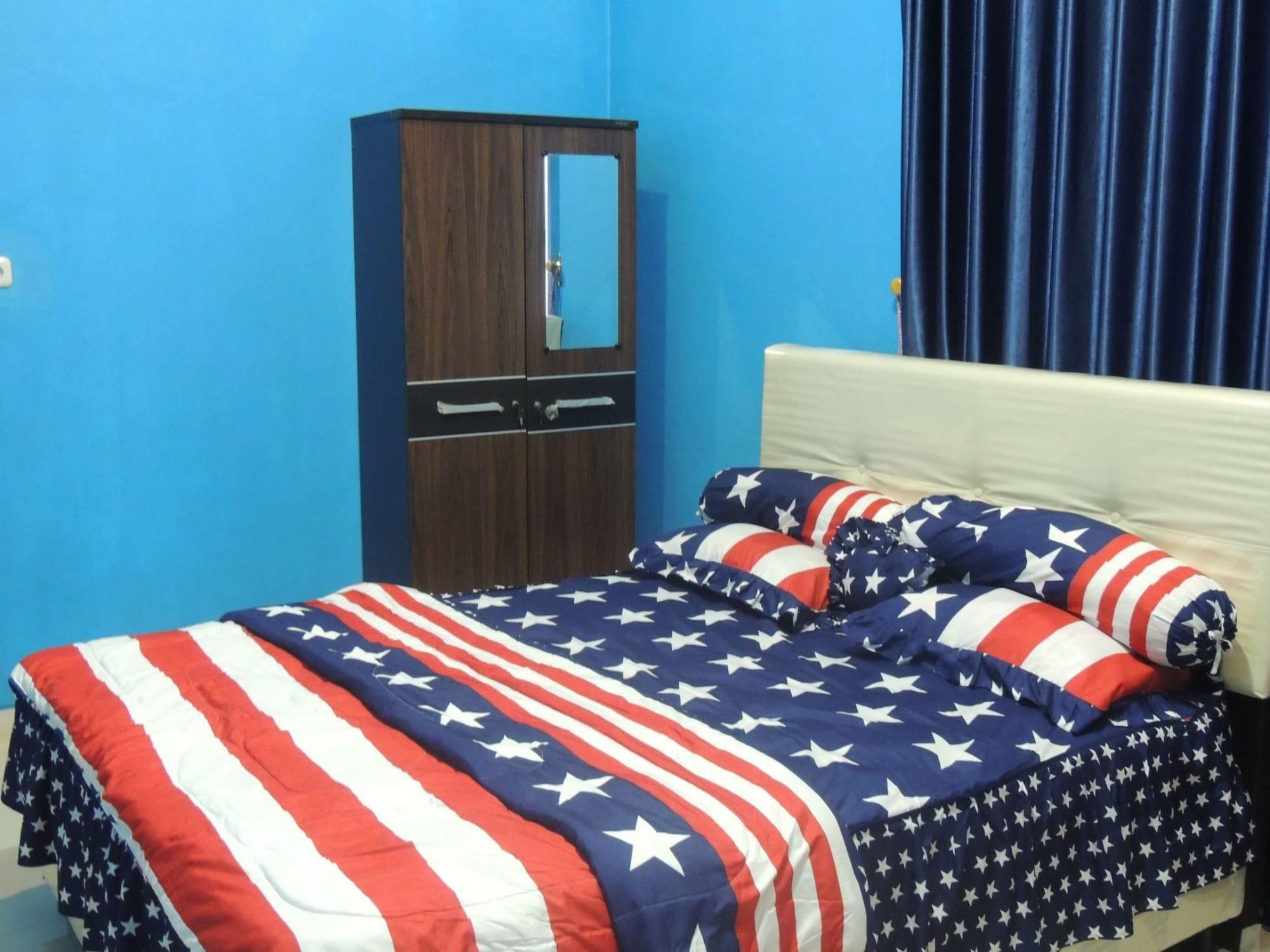 A bedroom with a bed covered in an American flag-themed blanket, a wooden wardrobe, and a blue curtain.