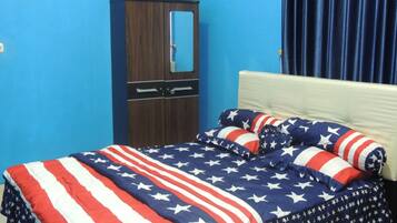 A bedroom with a bed covered in an American flag-themed blanket, a wooden wardrobe, and a blue curtain.