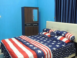 Un dormitorio con una cama cubierta con una manta con motivos de la bandera estadounidense, un armario de madera y una cortina azul.