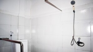 A small, white-tiled bathroom with a toilet, a shower head, and a handrail. - Charisma Residence (Surabaya)