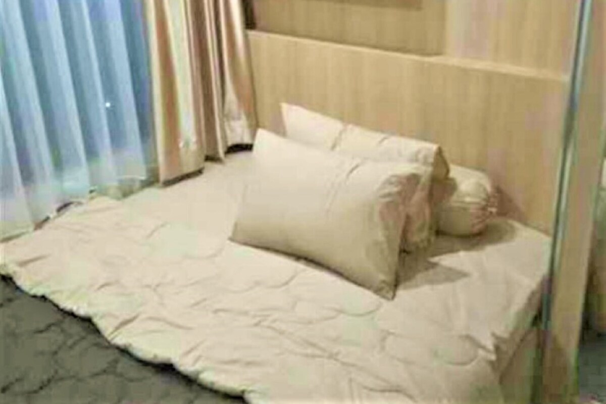 A bed with a beige bedspread and pillows, a wooden headboard, and a window with curtains.