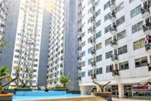 Un edificio residencial alto con varios balcones, un patio central con fuente de agua y zonas verdes circundantes.
