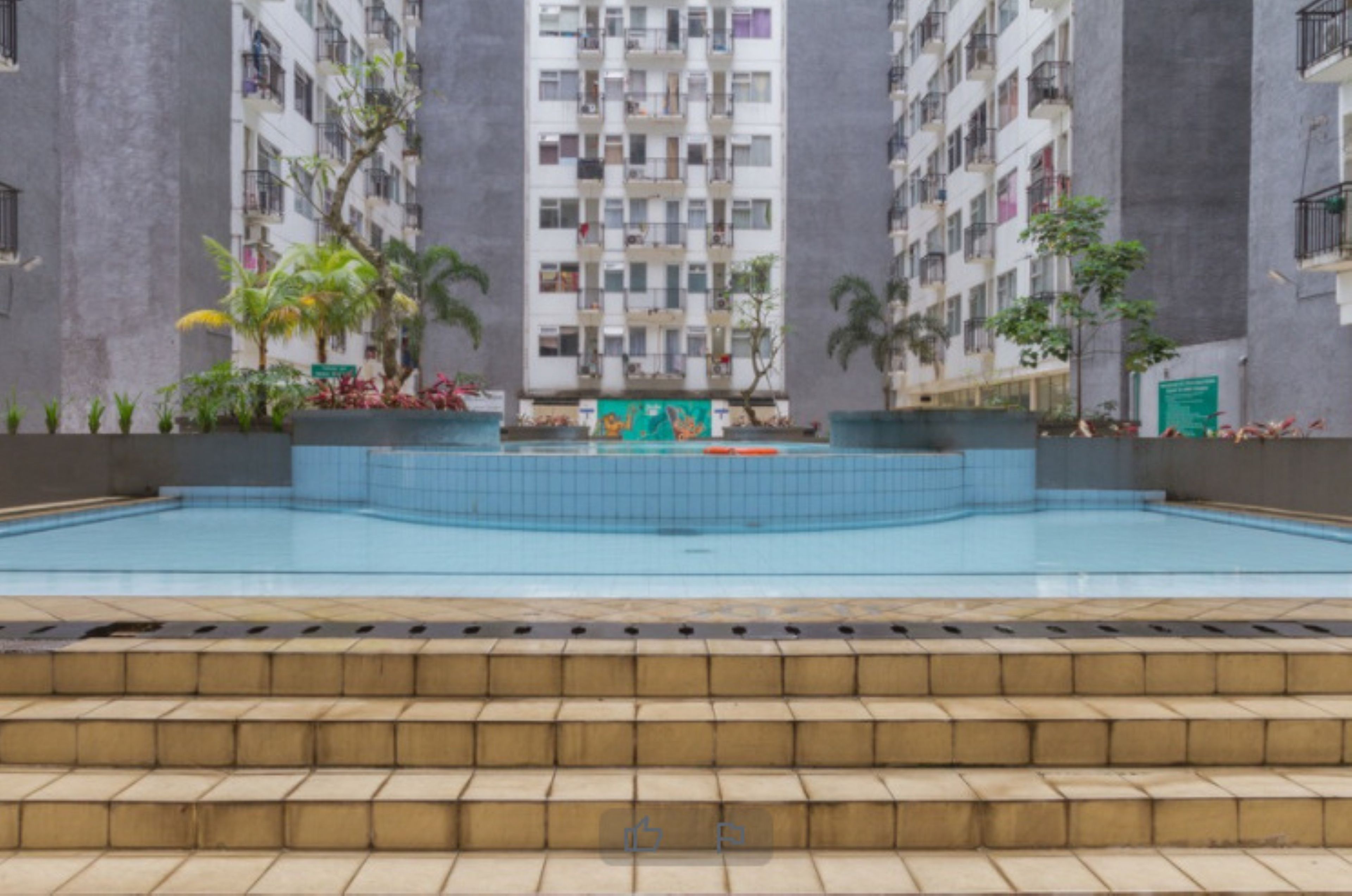 A swimming pool with tiled steps leading up to it, surrounded by a building with balconies and plants.