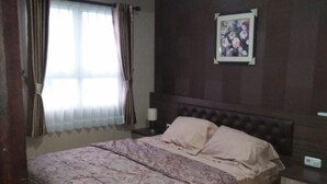 A bedroom with a double bed, a nightstand, a wall-mounted TV, and a window with curtains. - Apartment Gateway Pasteur Nazra Property (Cimahi)