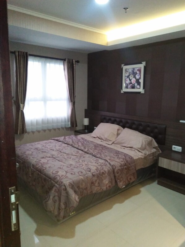 A bedroom with a double bed, a nightstand, a wall-mounted TV, and a window with curtains.